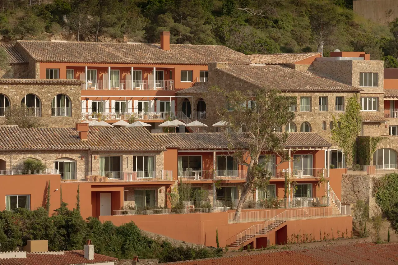 Finca Victoria luxury hotel on a hillside in Costa Brava, with terracotta walls and Mediterranean stonework surrounded by greenery.