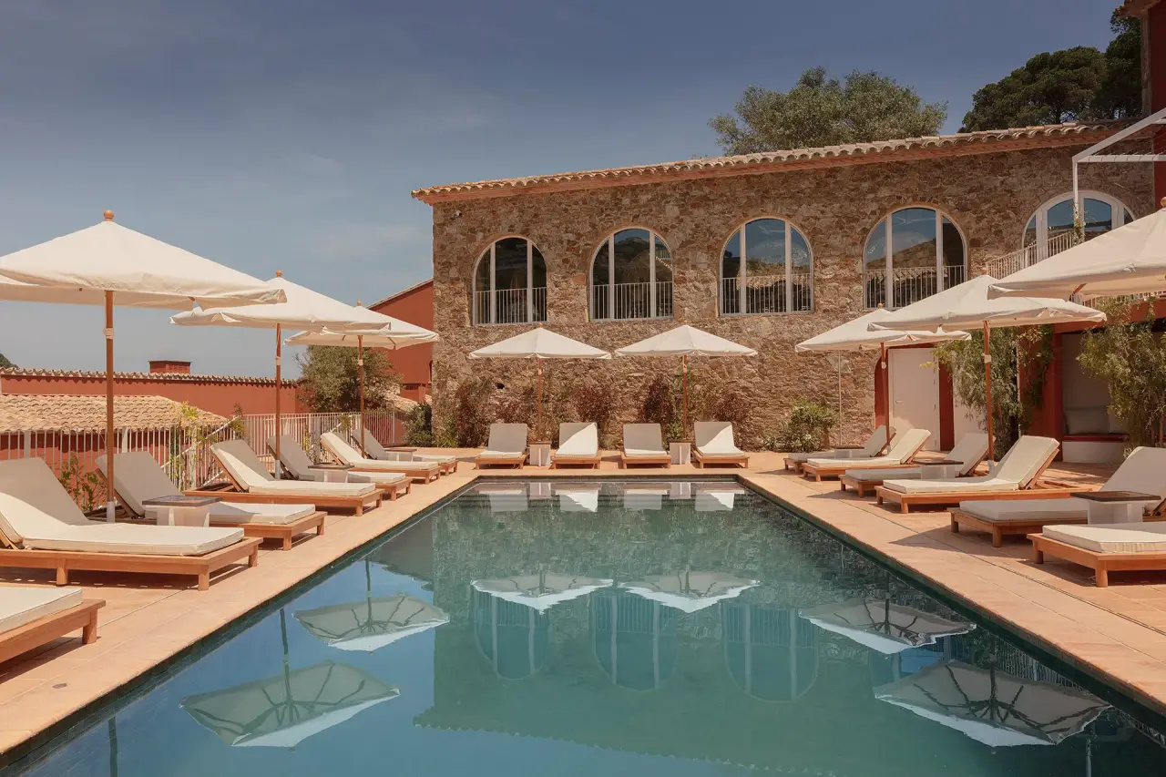 Outdoor pool at Finca Victoria with lounge chairs and umbrellas, surrounded by rustic Mediterranean architecture.