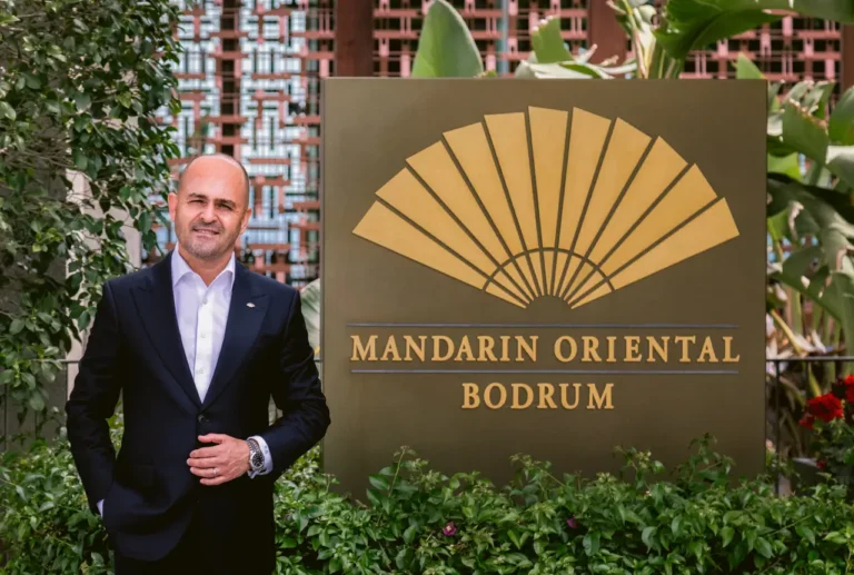 Volkan Öztürkler standing beside the Mandarin Oriental Bodrum sign, surrounded by lush greenery.