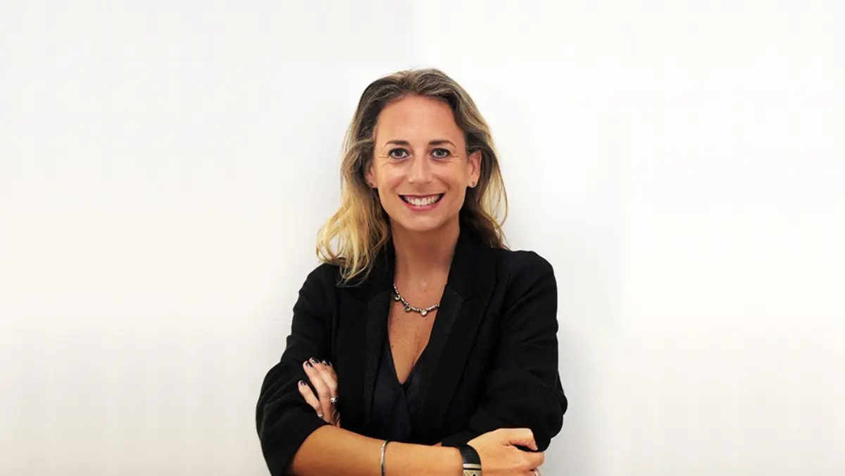 Brigitte Hidalgo smiling confidently with arms crossed, wearing a black blazer against a plain white background.