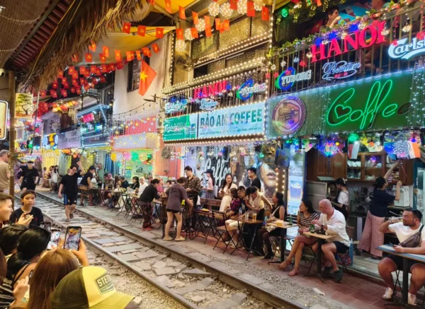 Nighttime scene of Hanoi Train Street with diners seated beside the illuminated railway track.
