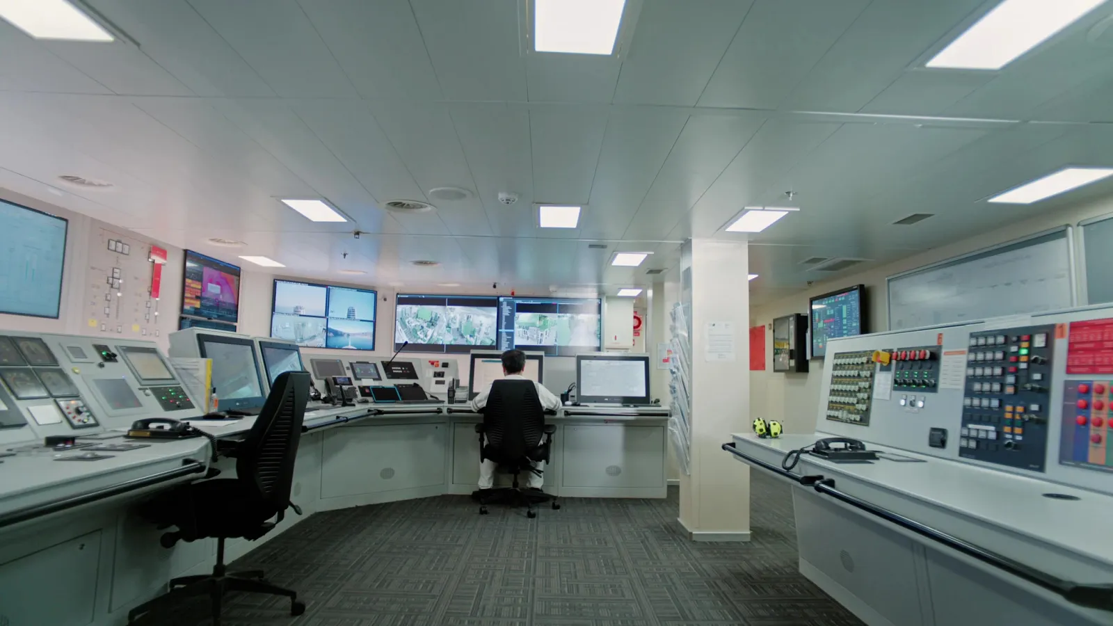 Behind-The-Scenes Cruise Tour: Holland America Unlocks Ship Secrets 3 Cruise ship crew member monitoring multiple screens and control panels inside a modern engine control room.