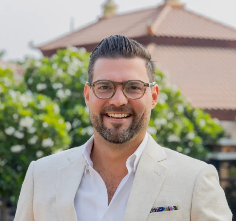 Appointments 7 Micheal Robinson in a light beige suit with glasses, standing outdoors in front of greenery and tiled-roof buildings.