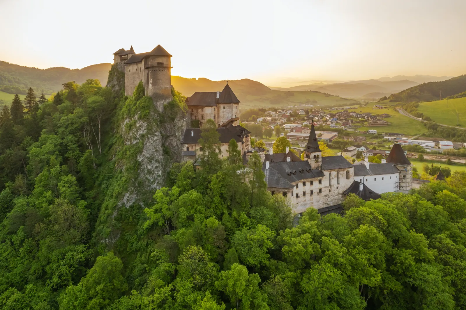 Spain Travel Trends 2025: Oviedo, Bilbao, And Rouen Shine As Cool Summer Escapes 5 Medieval Orava Castle perched on a rocky hilltop surrounded by green forests and a village landscape in Slovakia at sunset.