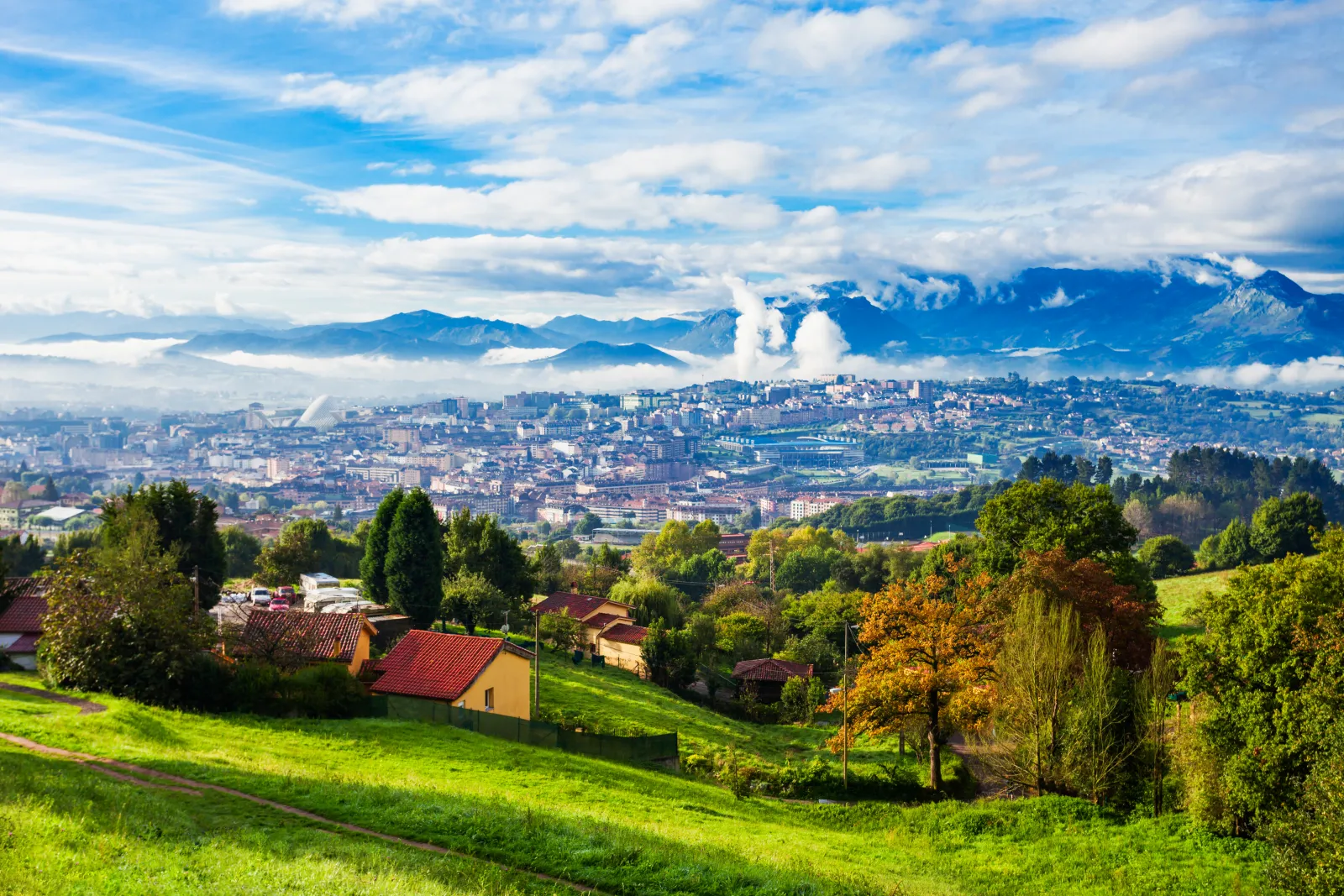 Spain Travel Trends 2025: Oviedo, Bilbao, And Rouen Shine As Cool Summer Escapes 4 Panoramic view of Oviedo, Spain, with lush green hills in the foreground and misty mountains in the background.