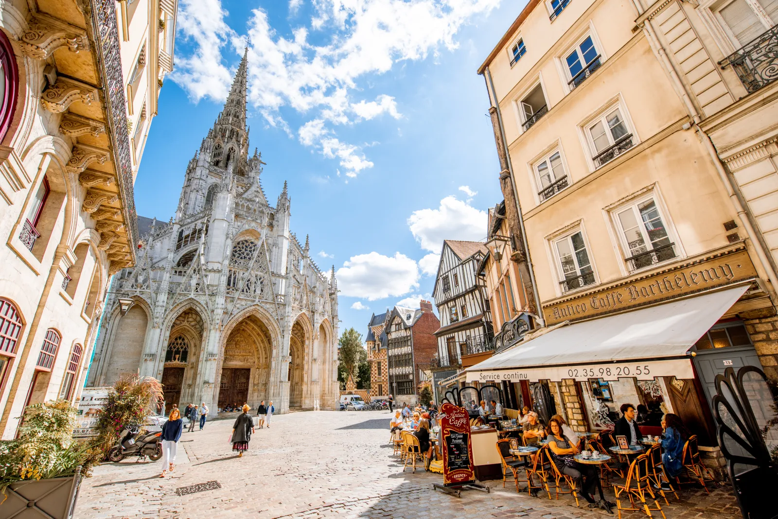 Spain Travel Trends 2025: Oviedo, Bilbao, And Rouen Shine As Cool Summer Escapes 3 ALT Text:Historic city square in Rouen, France, featuring a Gothic cathedral, half-timbered houses, and outdoor café seating under a sunny sky.