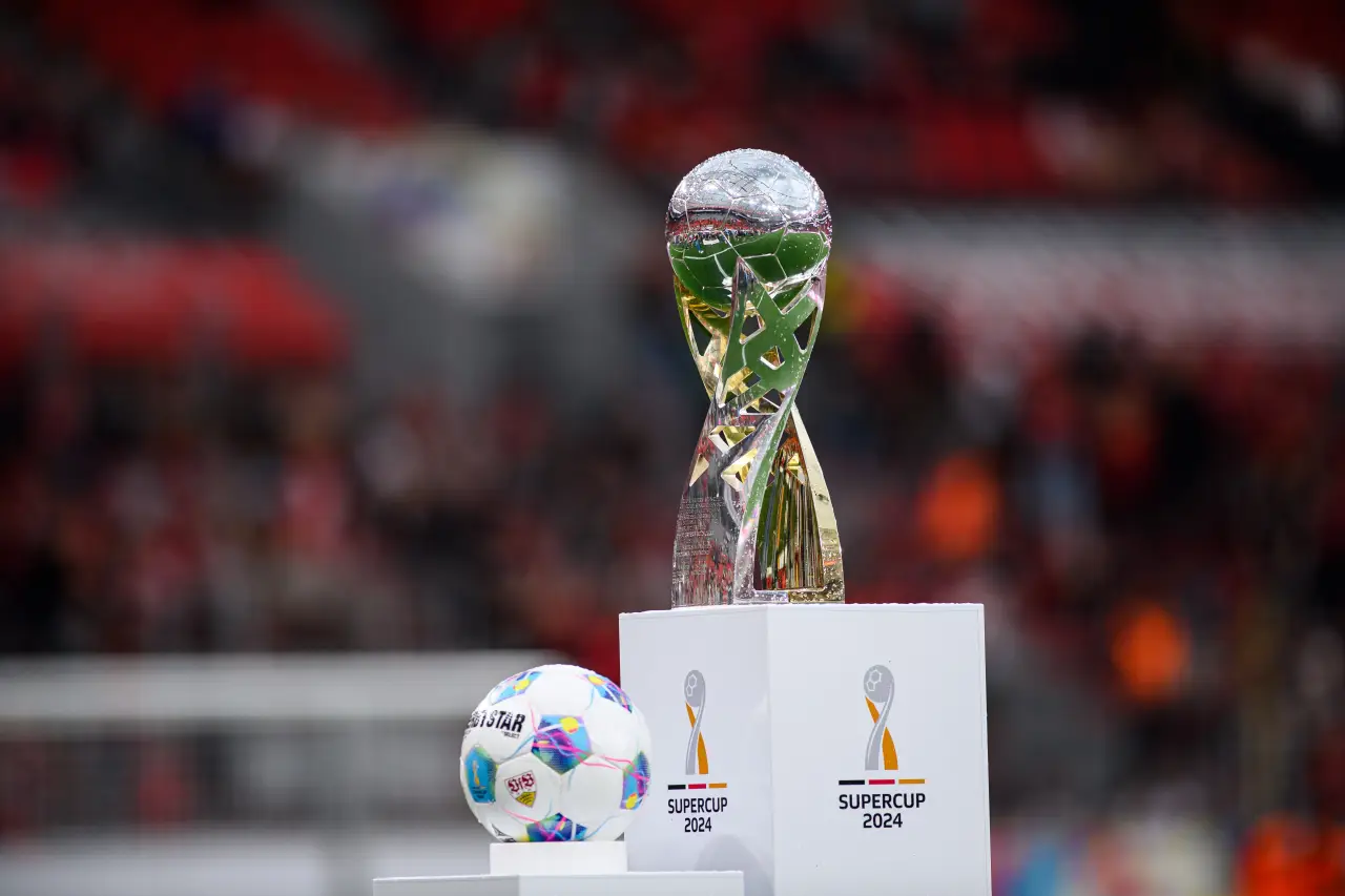 The UEFA Super Cup 2024 trophy and official match ball displayed on a podium before kickoff, with blurred stadium crowd in the background.