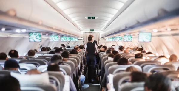 View of a crowded airplane cabin with passengers seated and flight attendants in the aisle.