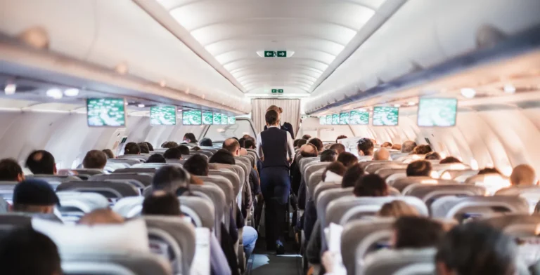 View of a crowded airplane cabin with passengers seated and flight attendants in the aisle.