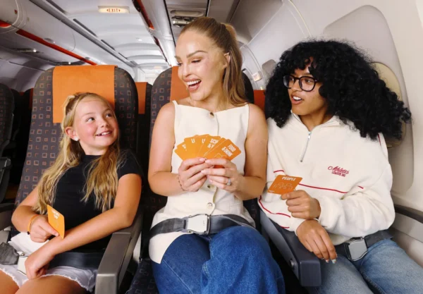 Home 8 A smiling woman and two children playing easyJet’s Airplane Mode card game on an airplane, sitting in orange-trimmed seats and engaging in conversation.