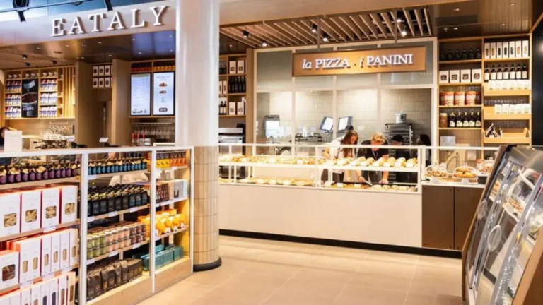 Interior of Eataly at Schiphol Airport featuring Italian food retail shelves and a counter serving pizza and panini.