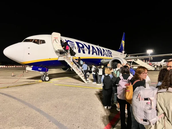 Home 9 Passengers with backpacks and hand luggage boarding a Ryanair airplane at night via stairs on the tarmac.