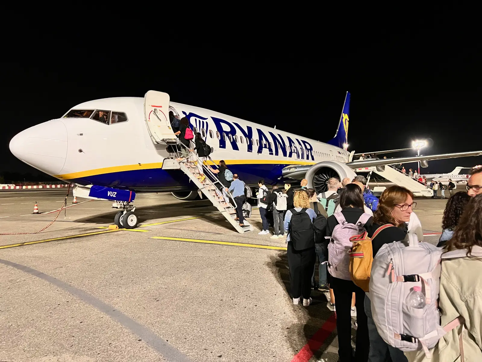 What Ryanair’s New Digital Boarding Pass Rule Means for You 27 Passengers with backpacks and hand luggage boarding a Ryanair airplane at night via stairs on the tarmac.