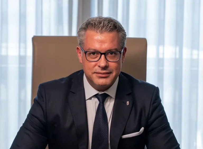 Portrait of Dimitrios Kotsifakos, newly appointed General Manager of The Ritz-Carlton, Amman, wearing a dark suit and tie, seated at his desk.