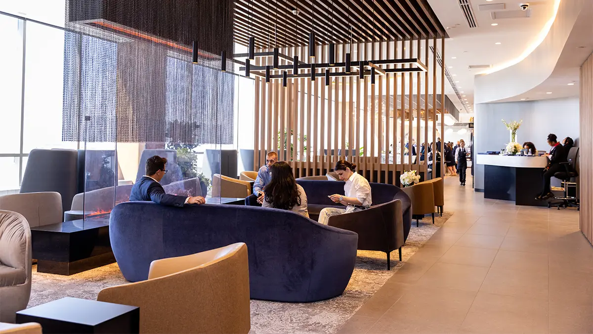 Passengers relax in a modern American Airlines airport lounge featuring contemporary seating, private areas, and a reception desk in the background.