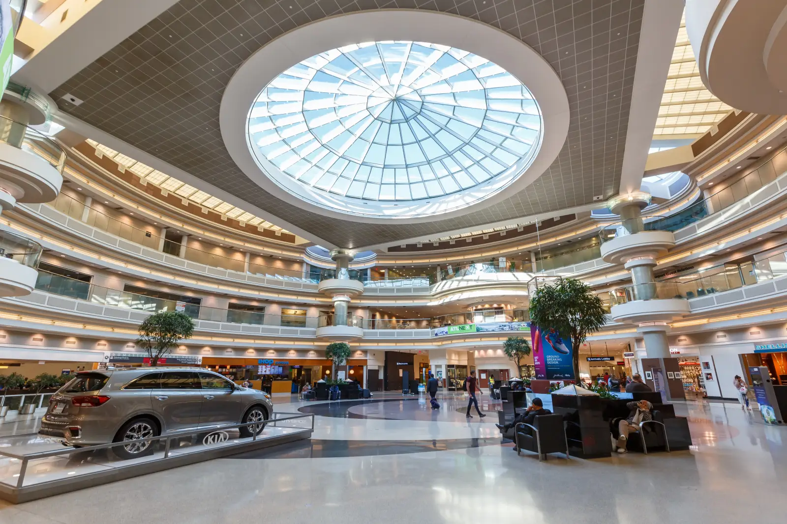 Interior of Hartsfield-Jackson Atlanta International Airport with a skylight dome, multiple retail levels, and travelers walking through the concourse.