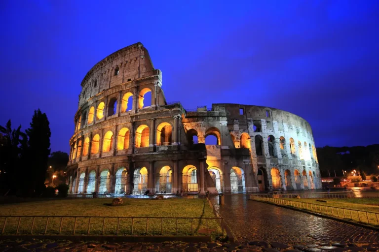 Tours 10 Colosseum in Rome illuminated at night with golden lights against a deep blue sky.