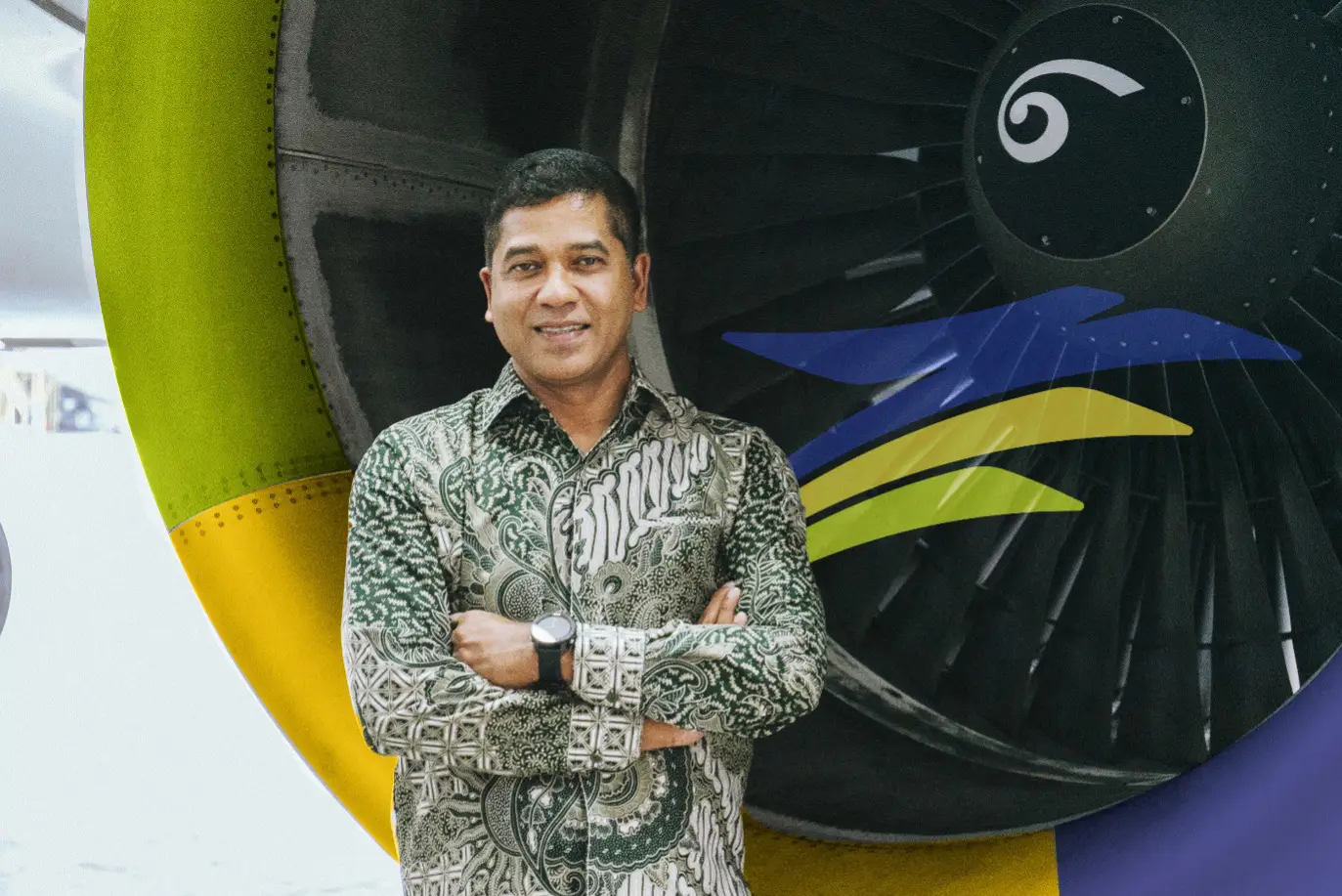 Datuk Bernard Francis, CEO of TransNusa Airlines, standing in front of a jet engine with colorful yellow, blue, and green accents.