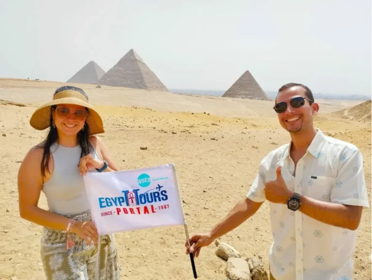 Two smiling executives at the Giza Pyramids in Egypt, holding an Egypt Tours Portal flag with the ASTA logo, under a sunny desert sky.