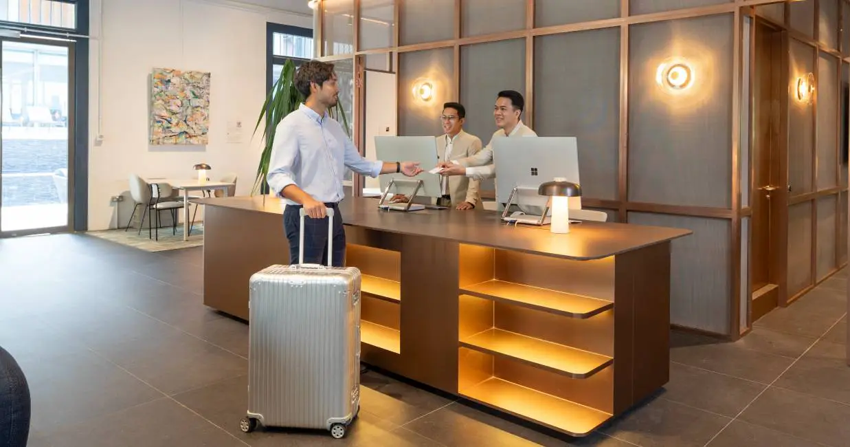Hotel guest checks in at the front desk of a Frasers Hospitality property, greeted by staff using modern reception facilities.