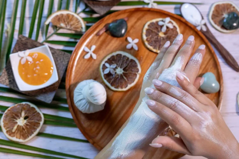 Hands receiving a luxurious spa treatment with white cream, surrounded by dried citrus slices, herbal poultice, and natural spa ingredients.