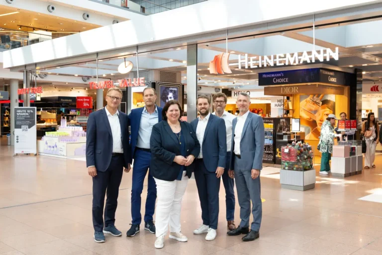 Group of business executives posing in front of a Heinemann Duty Free shop at Hamburg Airport.
