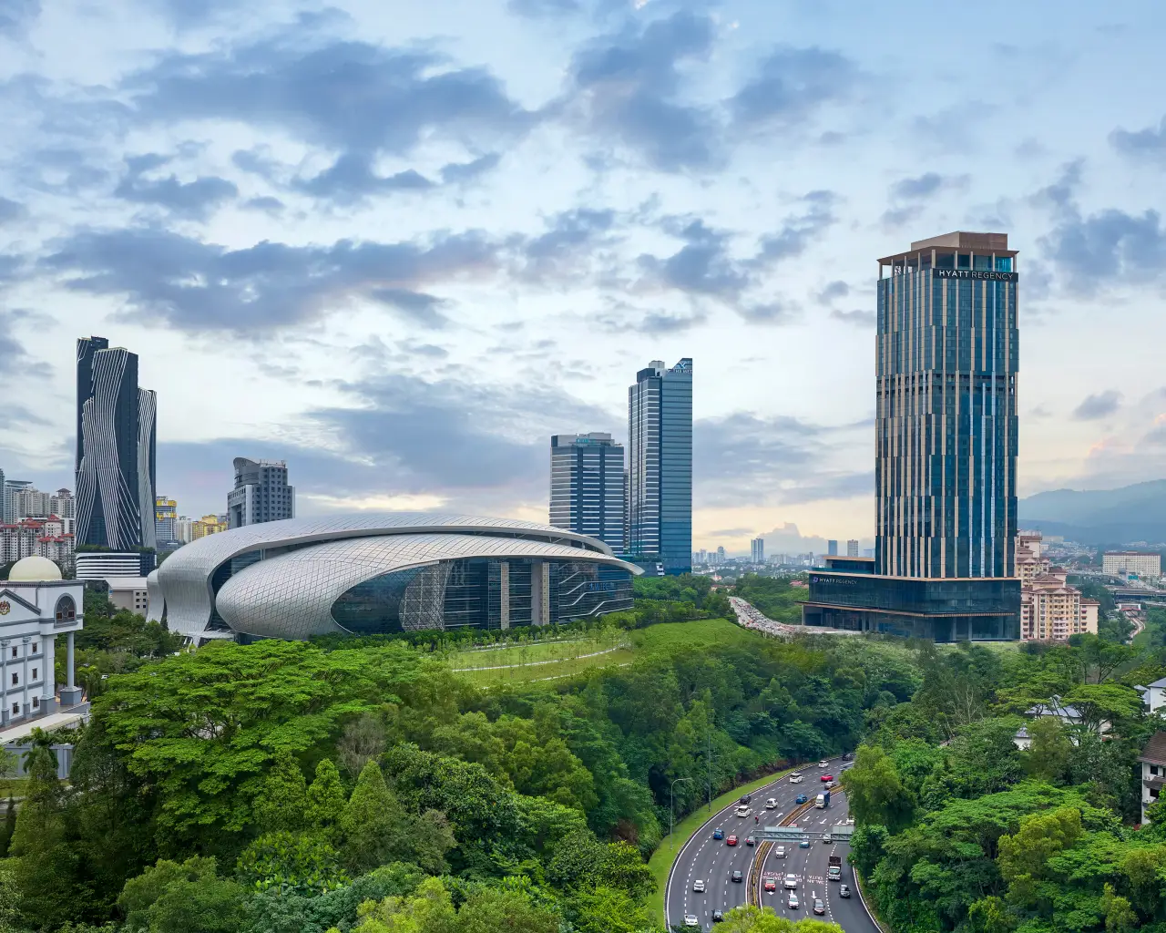 Skyline view of Kuala Lumpur featuring the new Hyatt Regency Kuala Lumpur at KL Midtown, with modern high-rise towers, MITEC convention center, and lush greenery in the foreground.