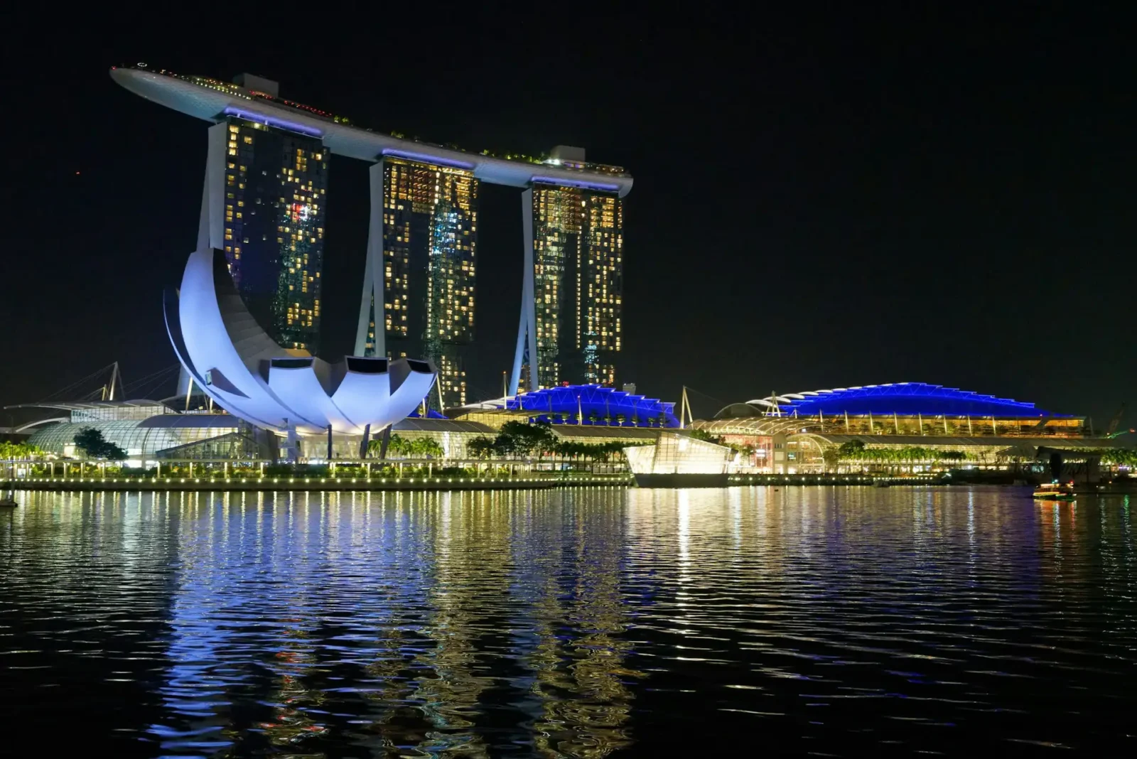 Night view of Marina Bay Sands and the ArtScience Museum in Singapore with reflections shimmering on the bay waters.