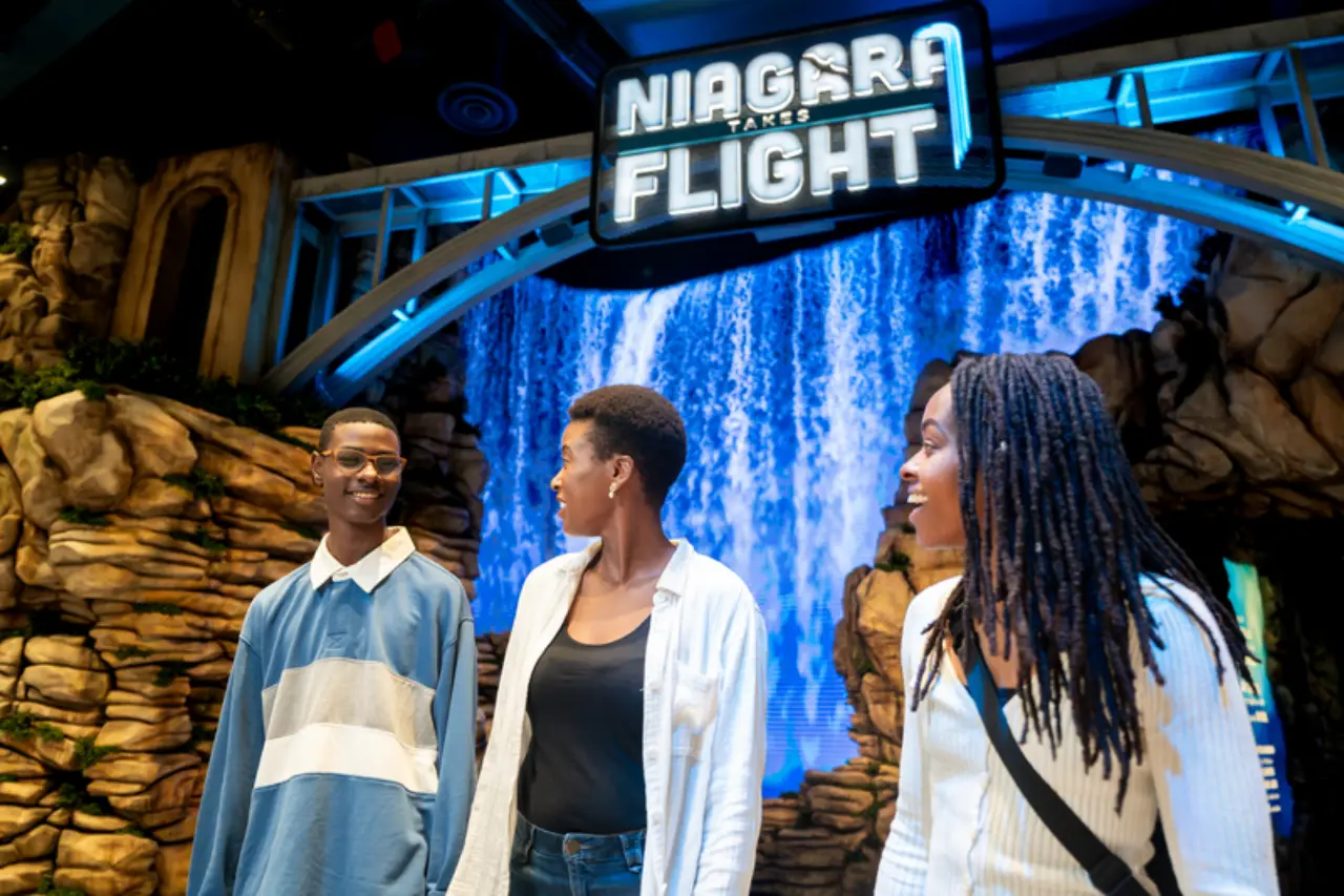 Visitors stand in front of the illuminated “Niagara Takes Flight” entrance marquee at Table Rock Centre in Niagara Falls, featuring a waterfall backdrop.
