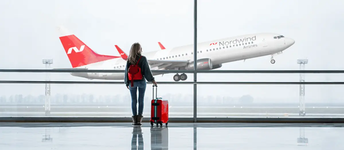Russia Launches Monthly Commercial Flights Between Moscow And Pyongyang 8 Traveler with red luggage watching a Nordwind Airlines plane take off from the airport.