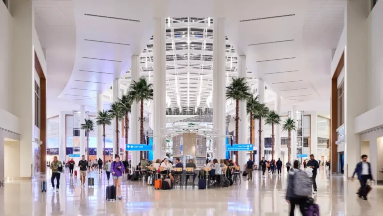 Retail 12 Interior of Orlando International Airport’s modern terminal with palm trees, travelers walking with luggage, and people seated in a central waiting area.
