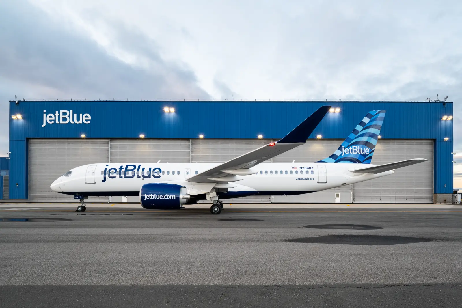 JetBlue Airbus A220-300 aircraft parked in front of blue hangar at airport