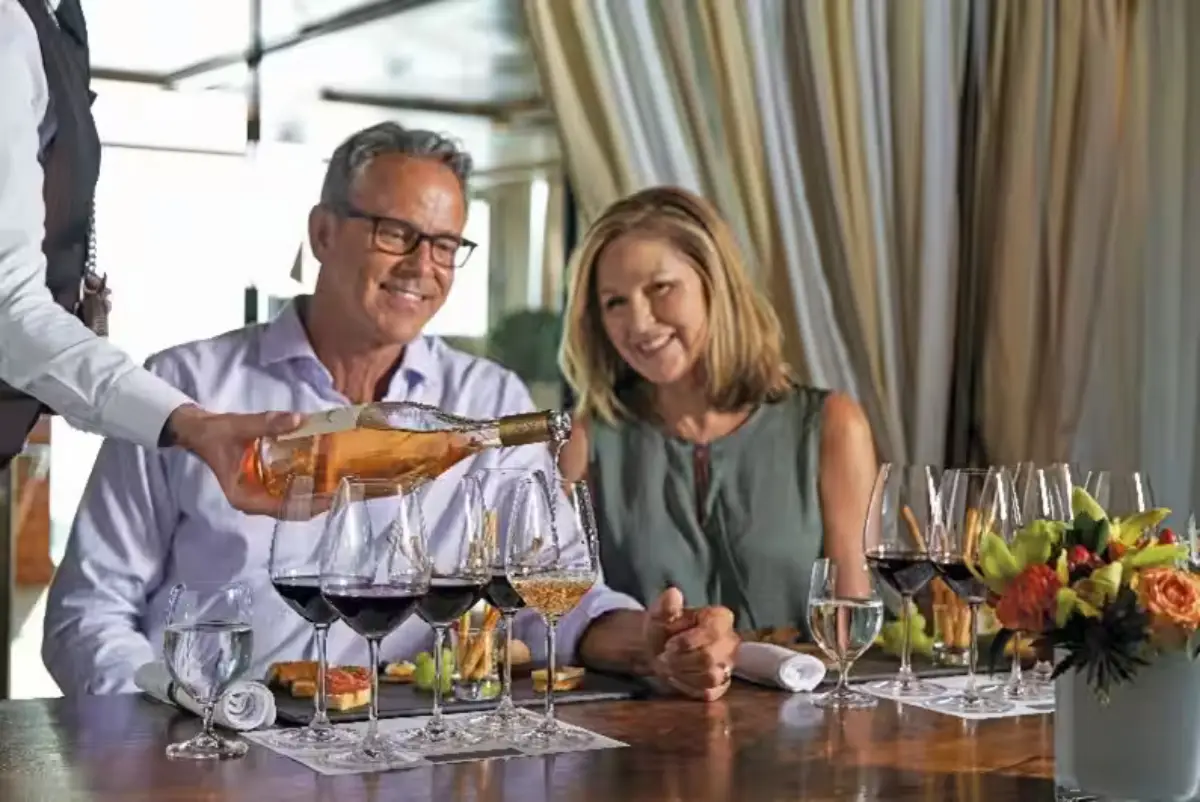 Couple enjoying wine service on a luxury cruise with glasses of red and white wine on the table.