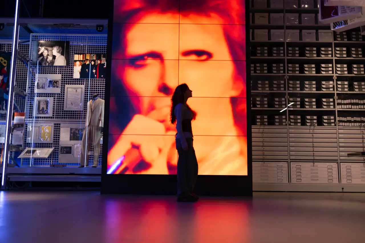 A visitor stands silhouetted in front of a large video screen showing David Bowie’s face at the V&A’s David Bowie Centre.