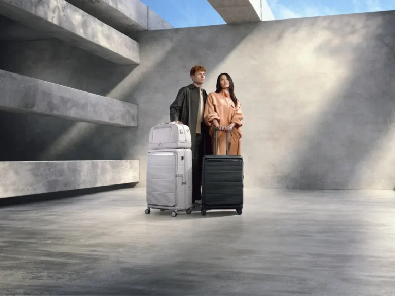 Two models stand in a minimalist concrete space with Samsonite Paralux suitcases, showcasing modular, eco-friendly travel gear in black and white.