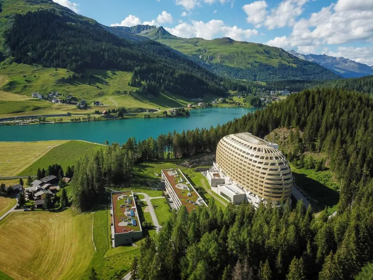 AlpenGold Davos hotel in Switzerland, surrounded by forested mountains and a lake in the Swiss Alps.