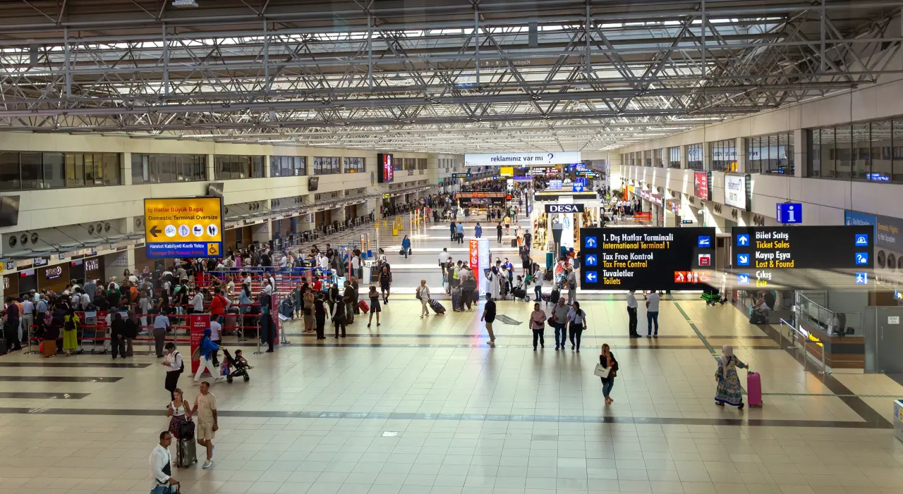 Passengers queuing at check-in counters inside Antalya Airport in Turkey.