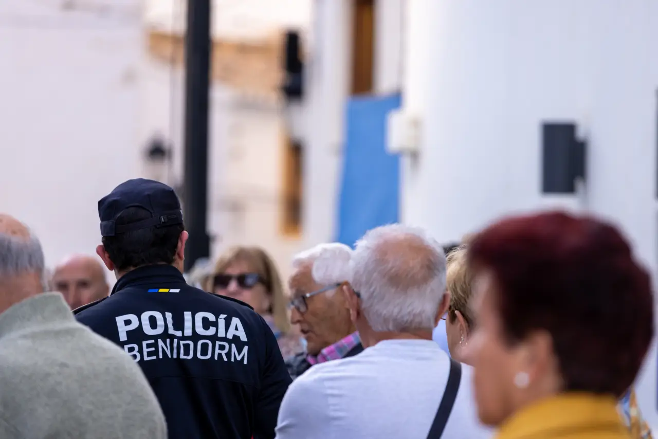 A Benidorm police officer stands among a group of elderly tourists on a city street, amid rising alcohol-related incidents involving British visitors.