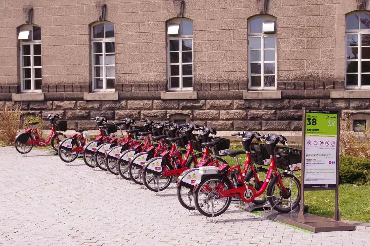 The Bike-Share Boom: Business Models &Amp; Funding Tips For First-Time Founders 2 Docked red rental bicycles lined up at a bike-share station with a sign in front of a stone building.