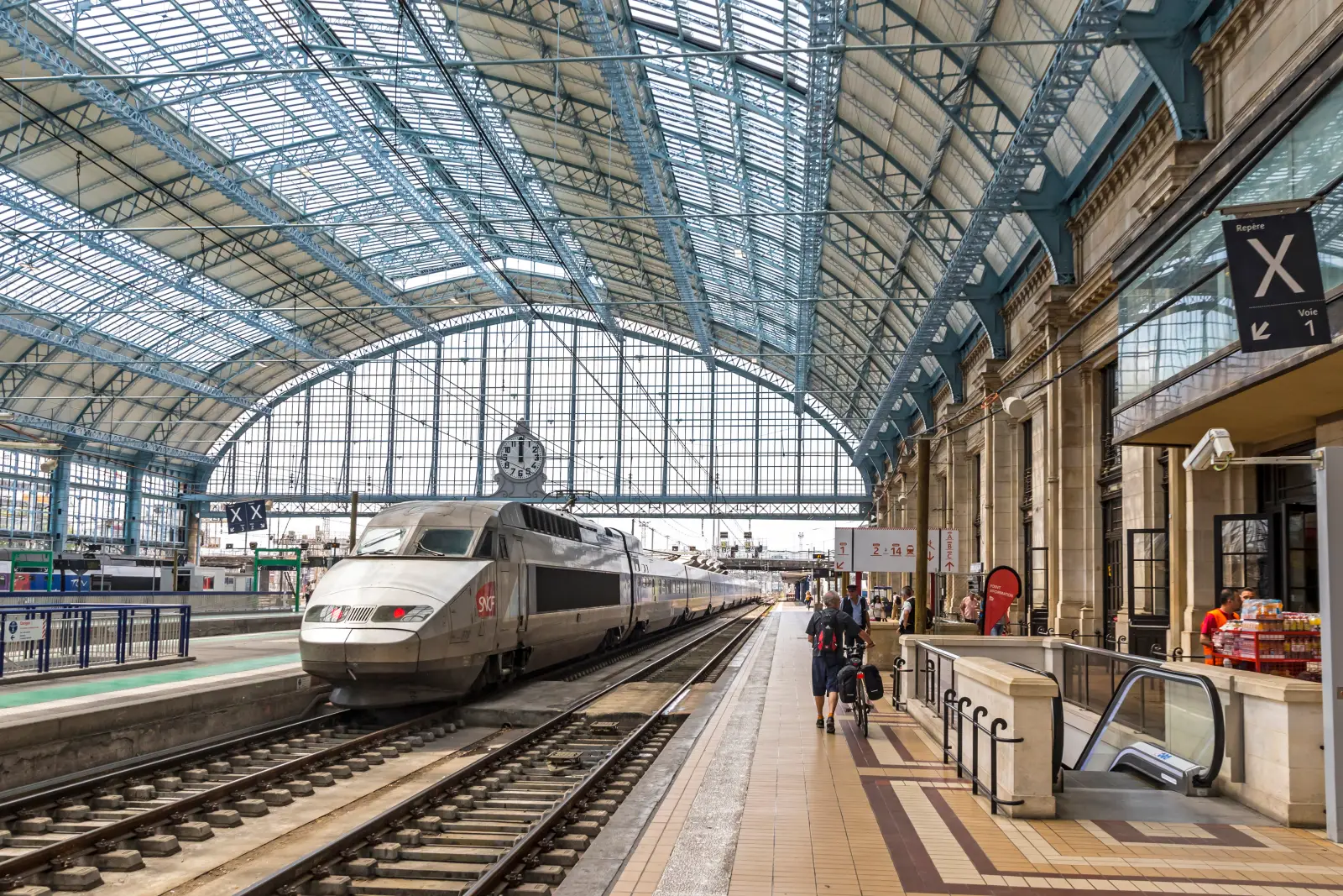 Southern France Rail Delays: SNCF Blames Arson for TGV Disruptions 39 SNCF high-speed TGV train at Bordeaux Saint-Jean station under the glass roof, with passengers waiting on the platform.