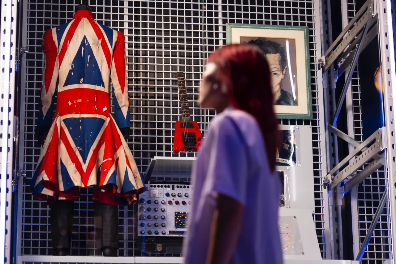 Get Up Close And Personal With David Bowie’s Legacy At London’s Victoria &Amp; Albert Museum 4 A visitor looks at David Bowie’s Union Flag frock coat, red guitar, and portrait on display at the V&A’s David Bowie Centre.