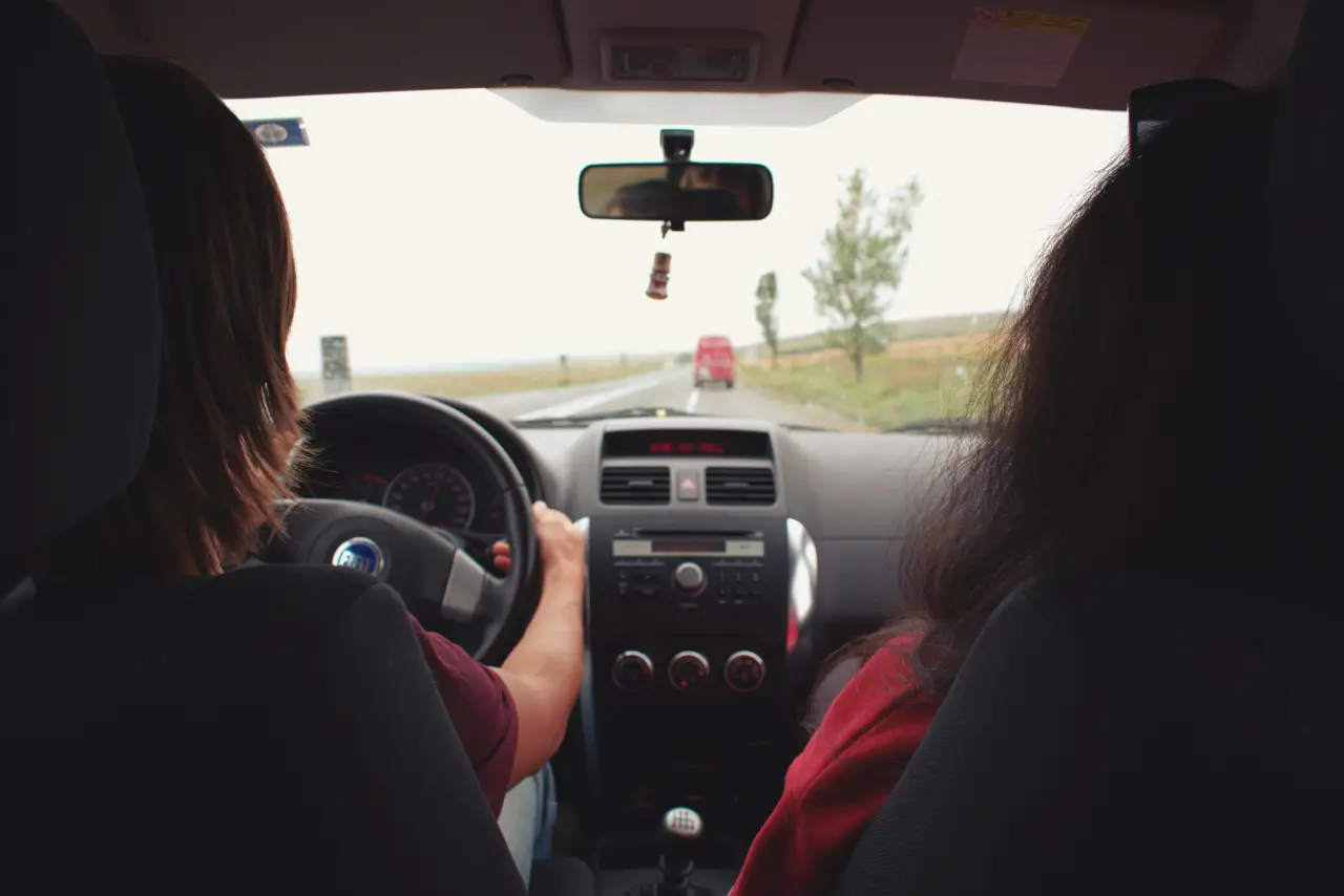 Two people driving on a rural road, viewed from the backseat of the car.