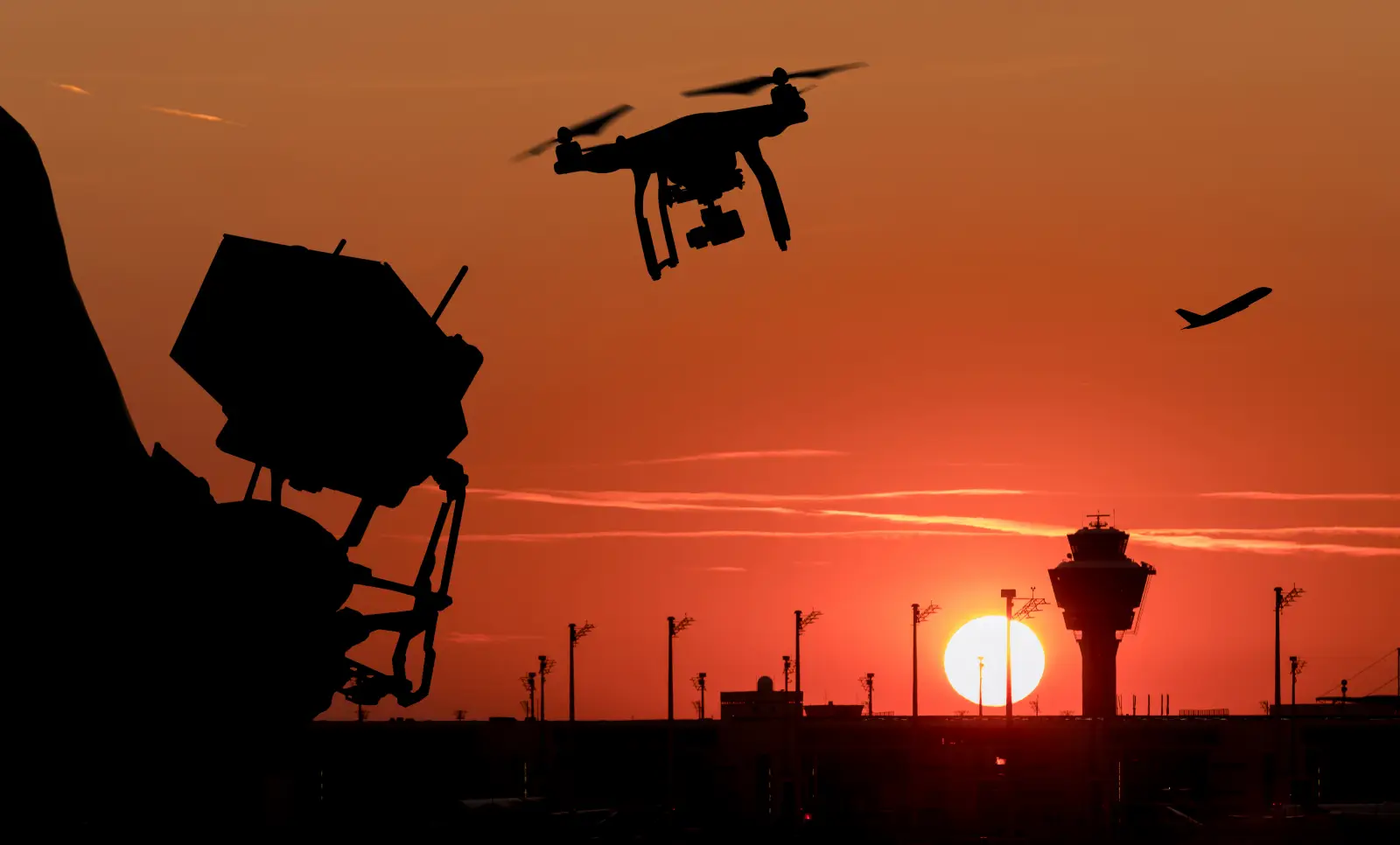 Drone flying near airport control tower and airplane at sunset