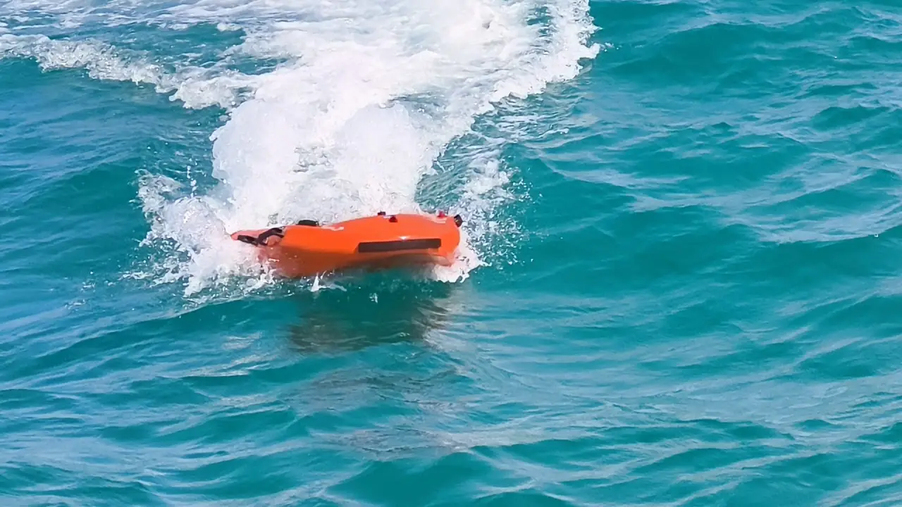 Orange Fasty remote-controlled lifeguard device speeding across blue seawater during a rescue test.