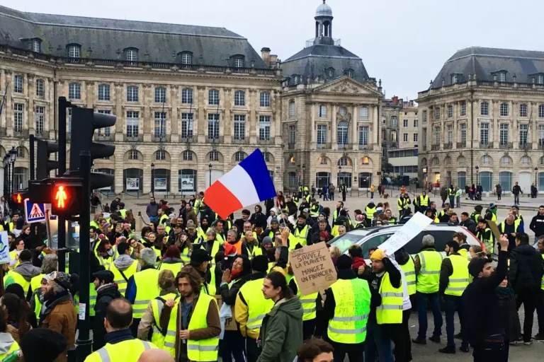 Protesters wearing yellow vests gather with French flags and signs during a demonstration in France, symbolizing national strikes and social unrest
