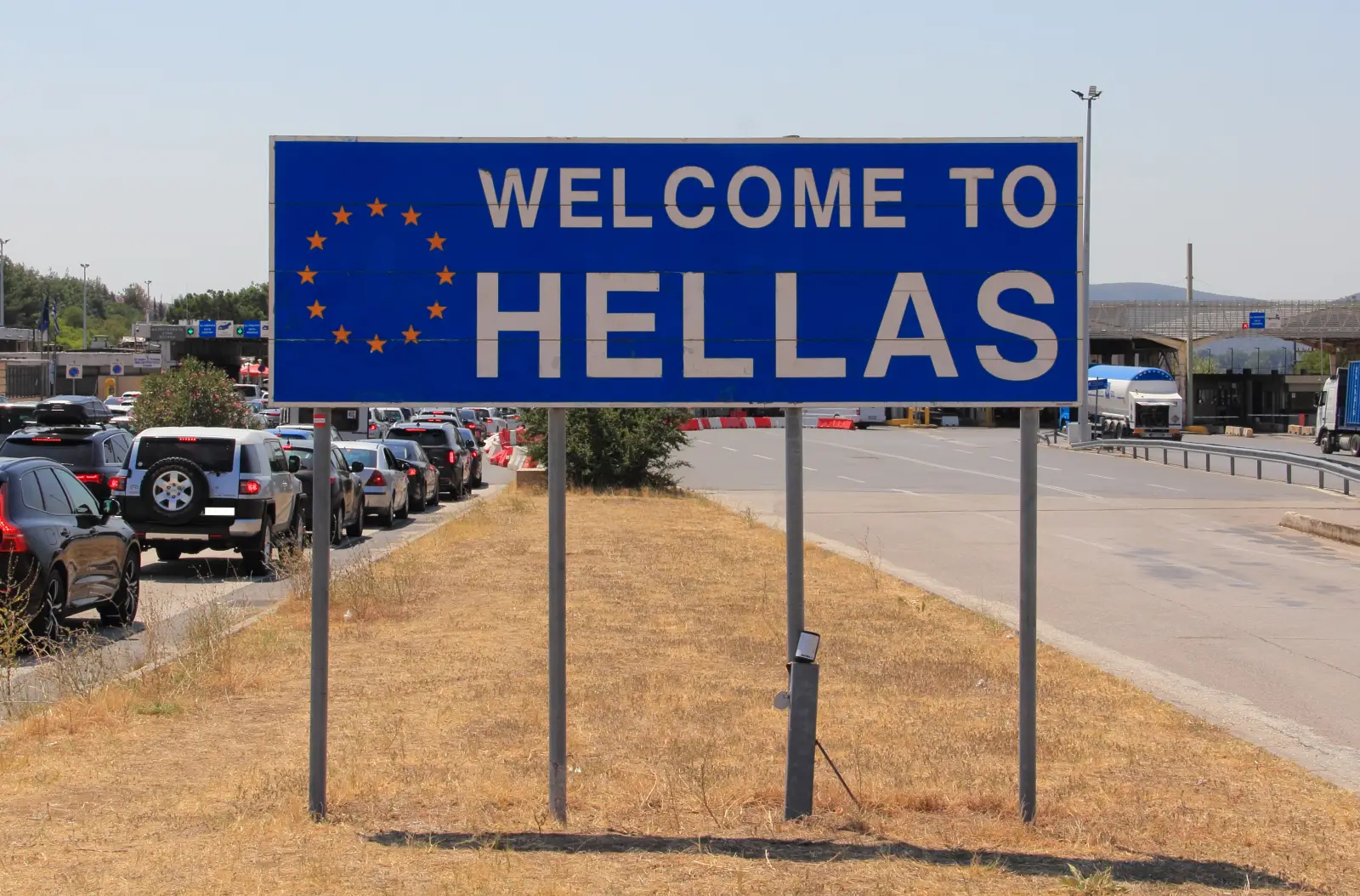 Welcome sign at Greece border with cars waiting in line