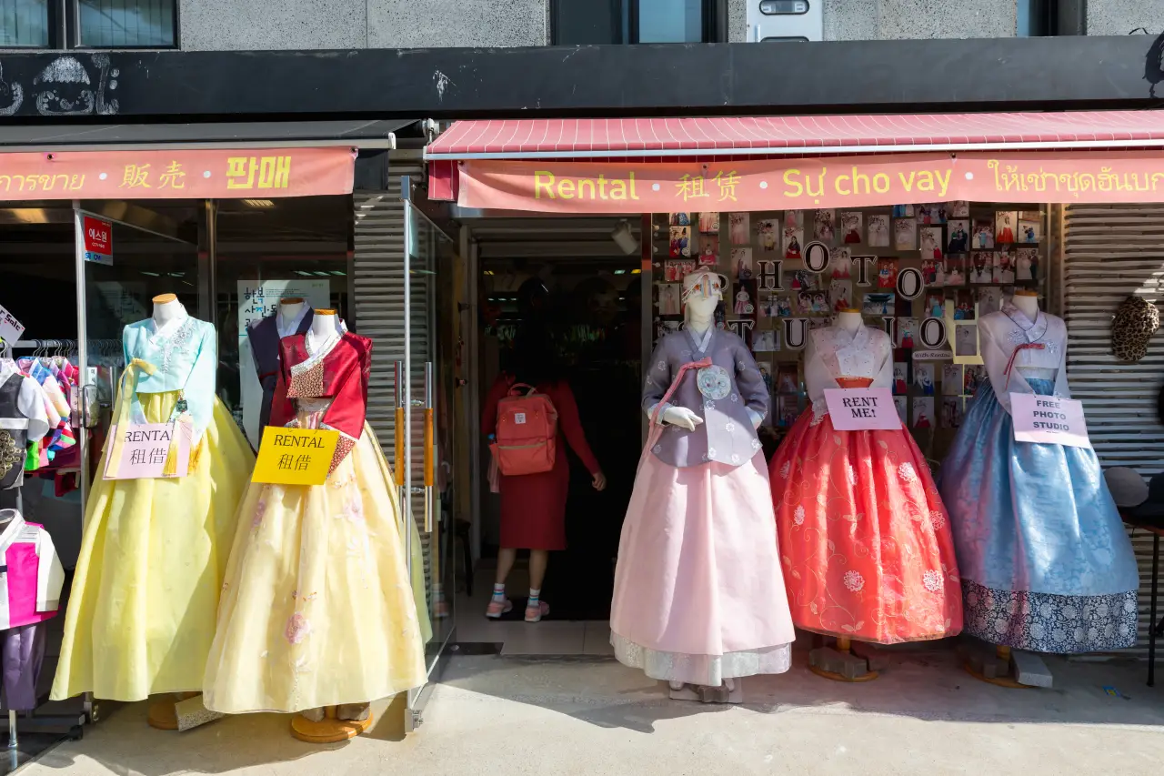 Display of colorful hanbok dresses outside a rental shop in Seoul, South Korea, with signs promoting rental services and photo studio access.