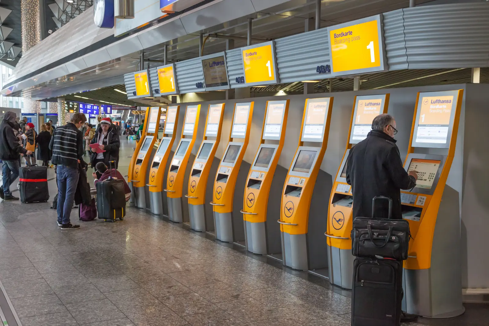 Passengers using Lufthansa self-service check-in kiosks at an airport terminal