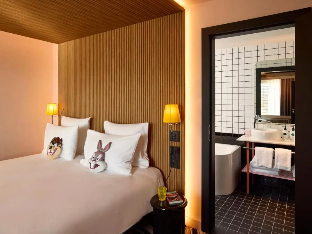 Cozy guest room at Mama Zurich with playful cartoon-themed pillows, modern wooden design, and en-suite bathroom with black-and-white tiles.