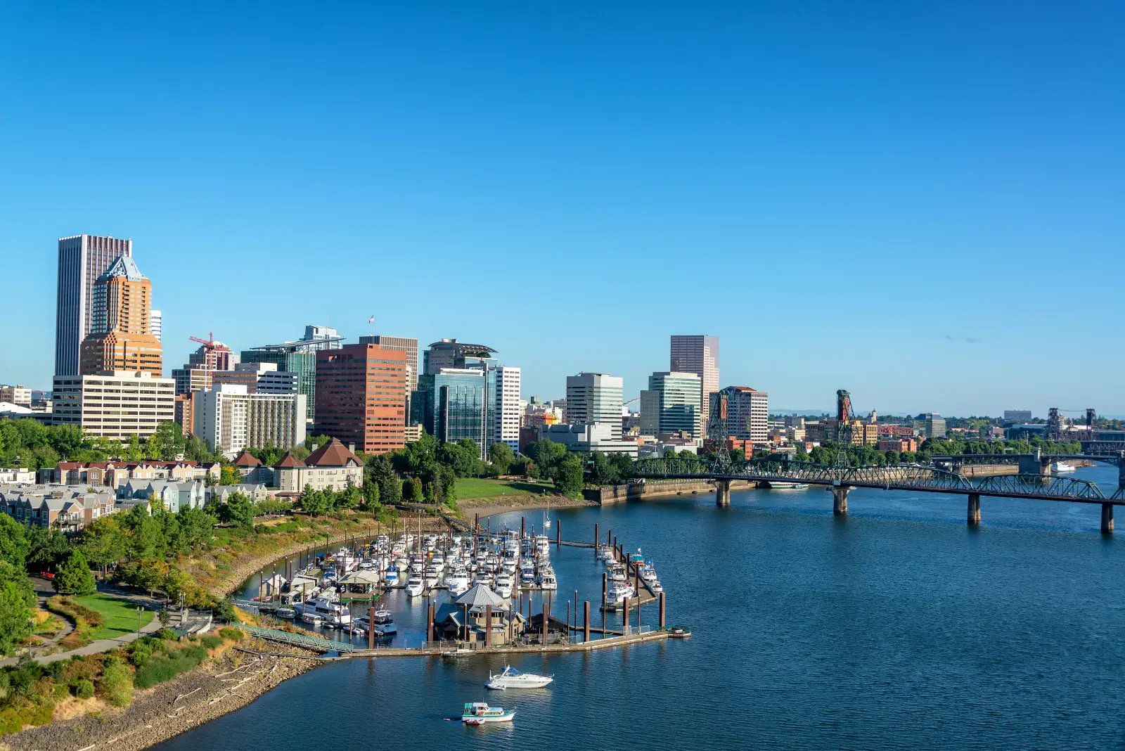 Downtown Portland skyline with waterfront marina and bridge over the Willamette River on a clear summer day.
